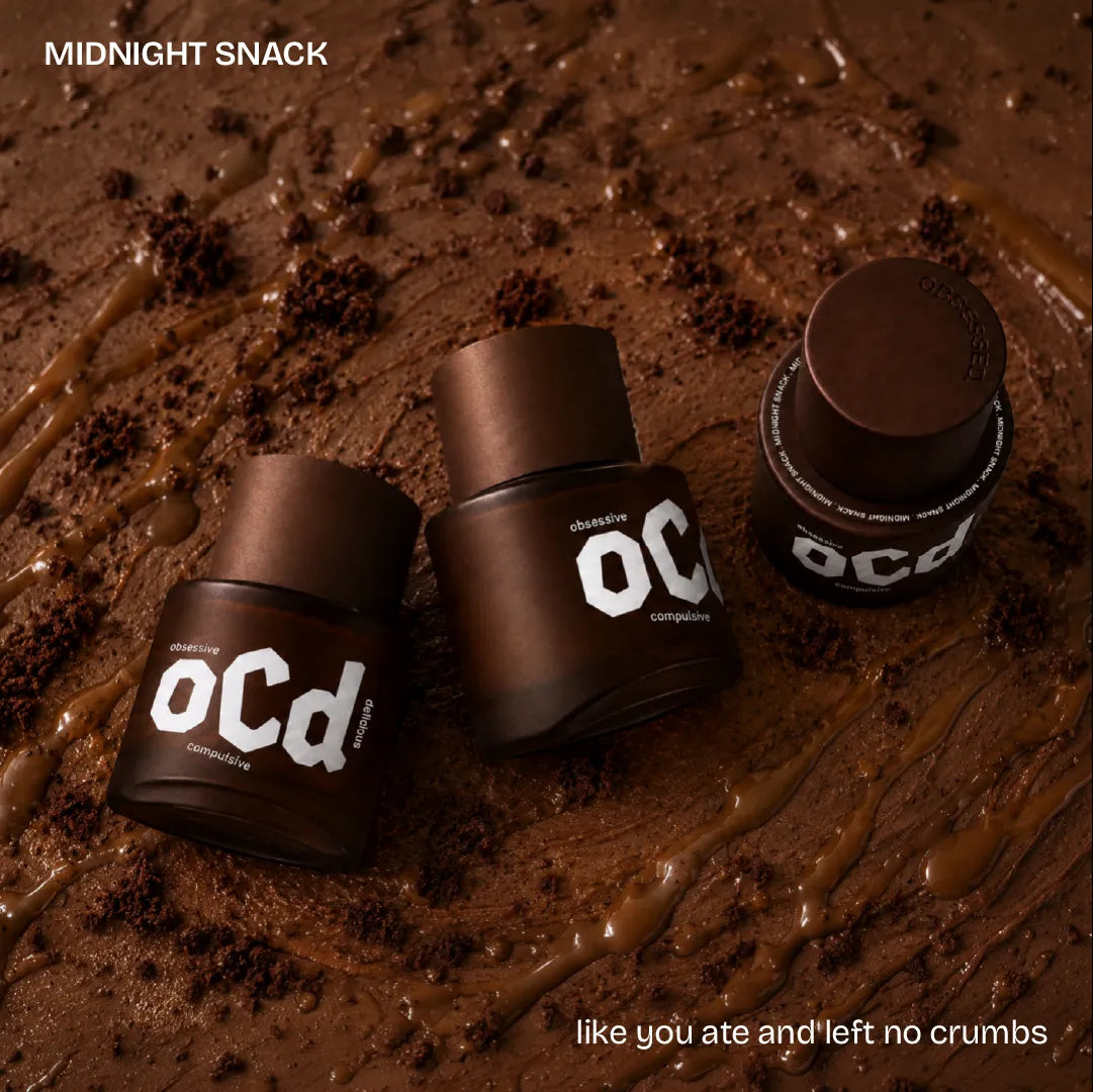 Three dark brown OCD perfumes arranged on a creamy chocolate surface with crumbs and drizzles. Text at top left reads 'MIDNIGHT SNACK' and at bottom right reads 'like you ate and left no crumbs'.