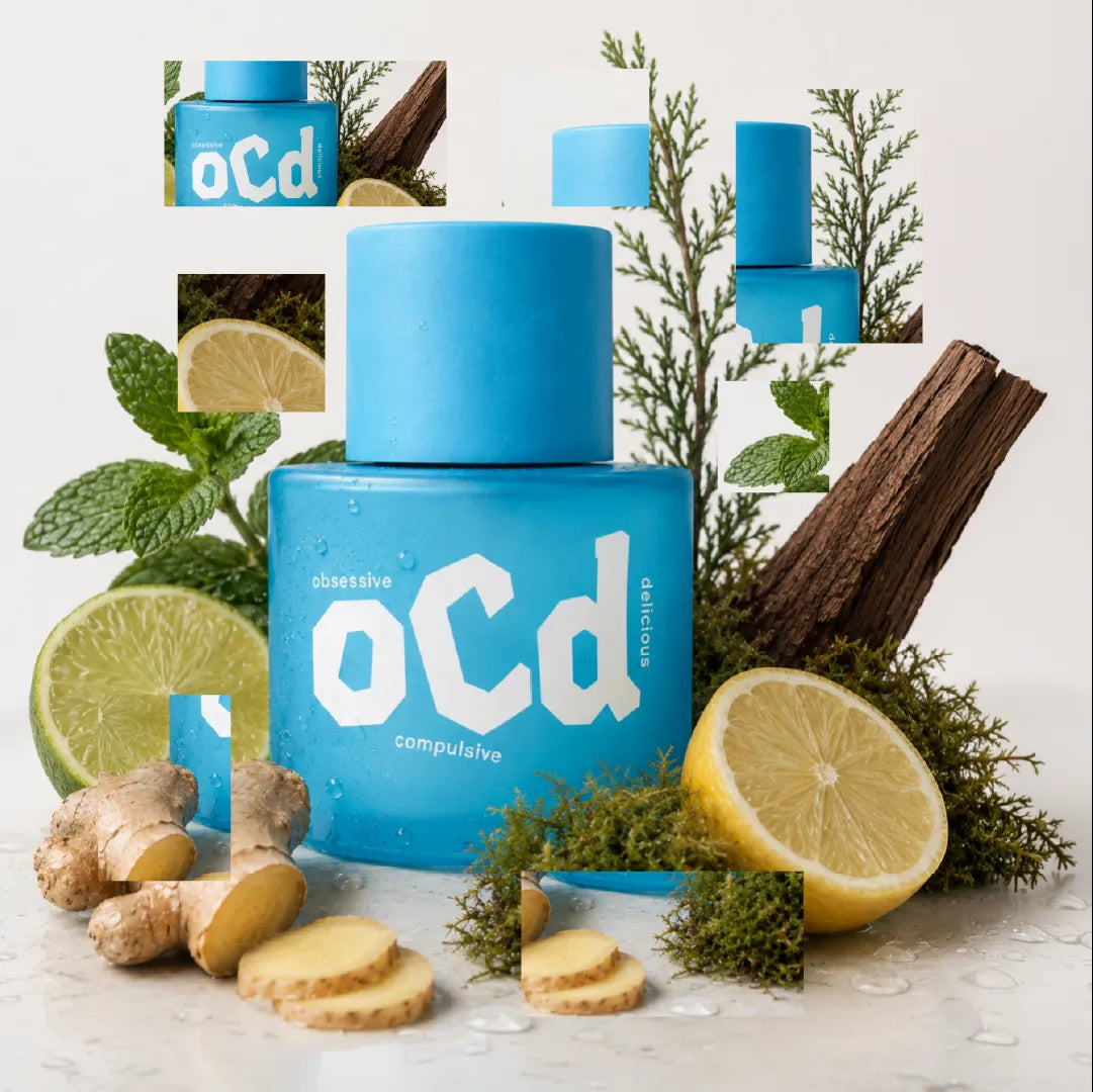 A blueperfume bottle labeled 'oCd' surrounded by natural ingredients including lemon slices, ginger roots, mint leaves, and a piece of wood, arranged on a white surface with a clean studio background.